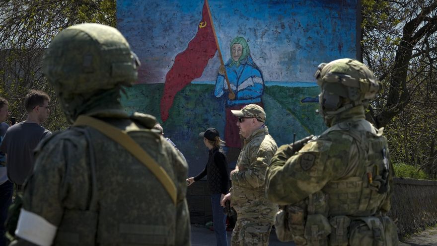 Militares rusos frente a un mural con una mujer ucraniana dibujada sosteniendo una bandera de la era soviética, en el territorio bajo el gobierno de la República Popular de Donetsk, en el este de Ucrania, el 30 de abril.
