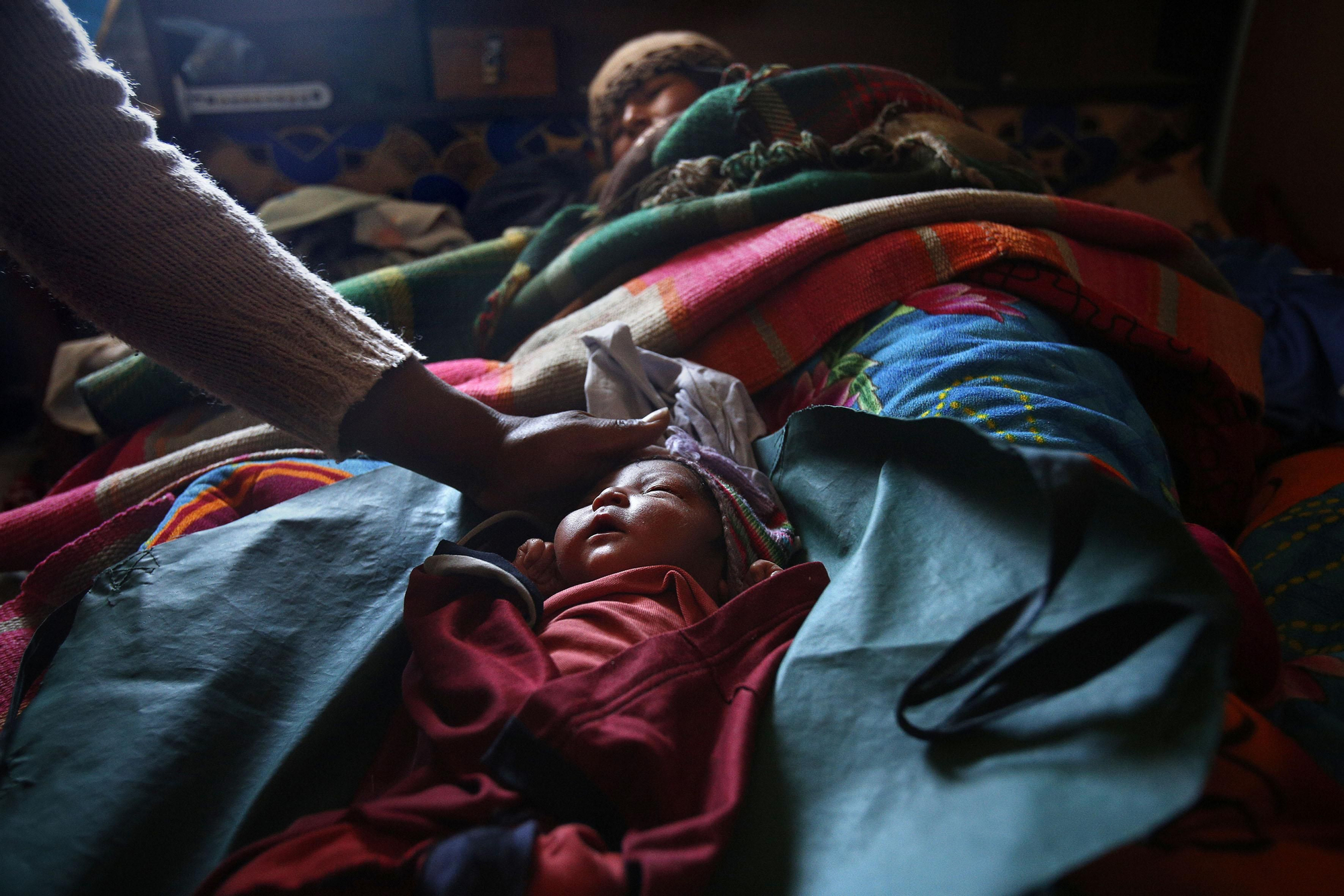 Elsa Quispe tumbada junto a su bebé de un día de edad en su casa en Patacamaya, mientras la auxiliar de enfermería Luz Maída lo tapa después de haberlo medido / Fotografía: Olmo Calvo