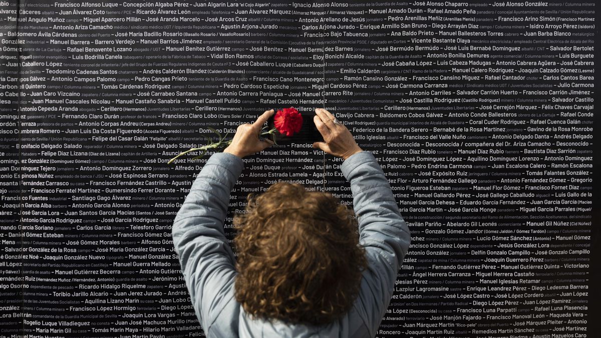 Archivo - Una mujer hace una foto del nombre de su familiar, colocado en un panel junto a los de las demás víctimas, durante el acto "institucional" de cierre de la fosa de Pico Reja. A 21 de febrero de 2023, en Sevilla (Andalucía, España). (Foto de archi