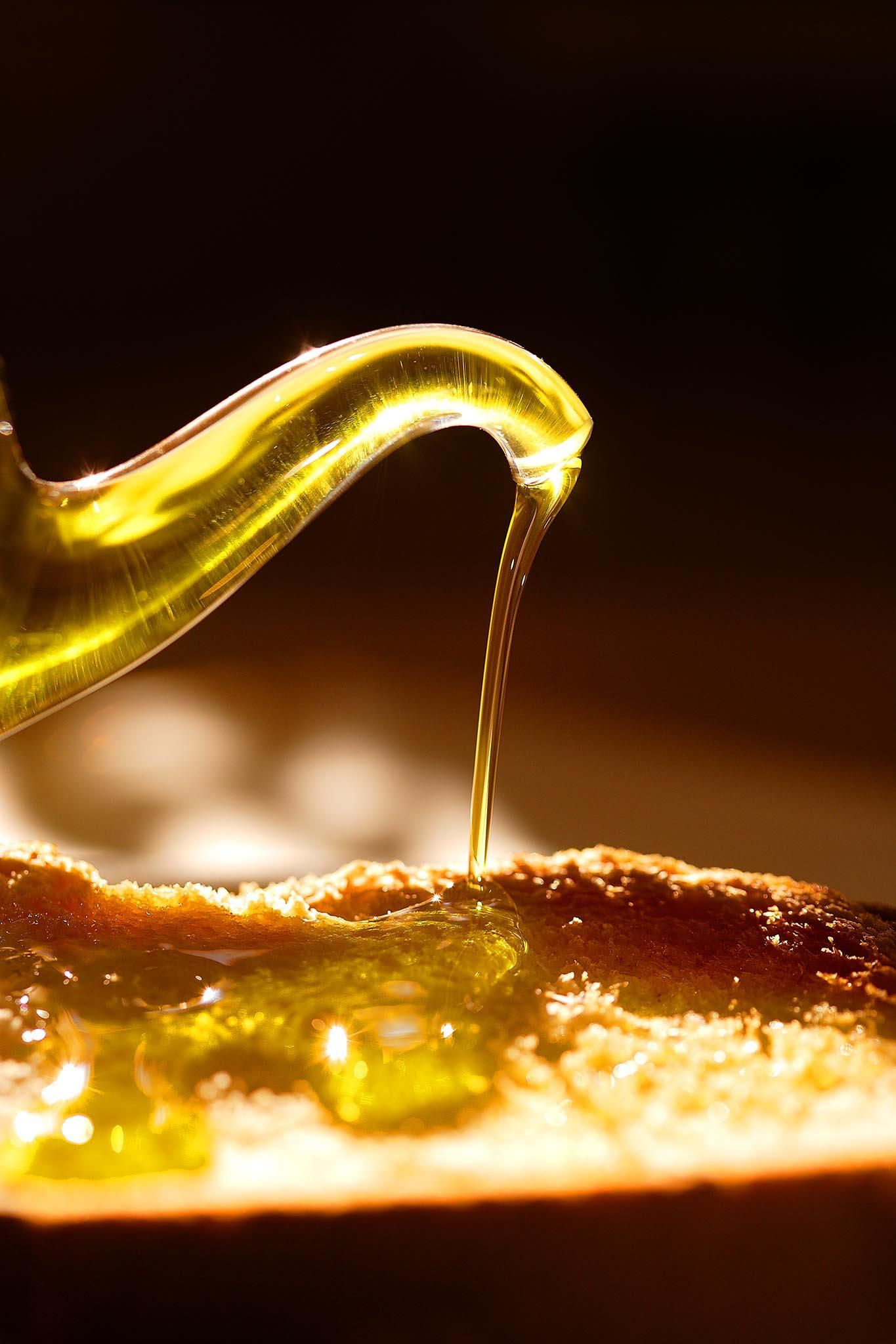 Detall d'un setrill abocant oli d'oliva damunt d'una torrada de pa de pagès