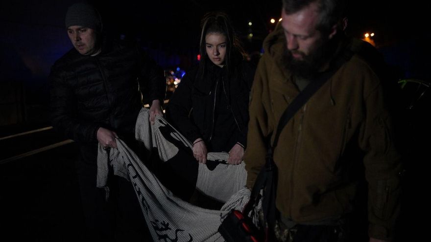 Un grupo de residentes por los bombardeos rusos de este jueves cerca del centro de Kiev, en el barrio de Shevchenkovsky, salen de la zona afectada con un perro herido.