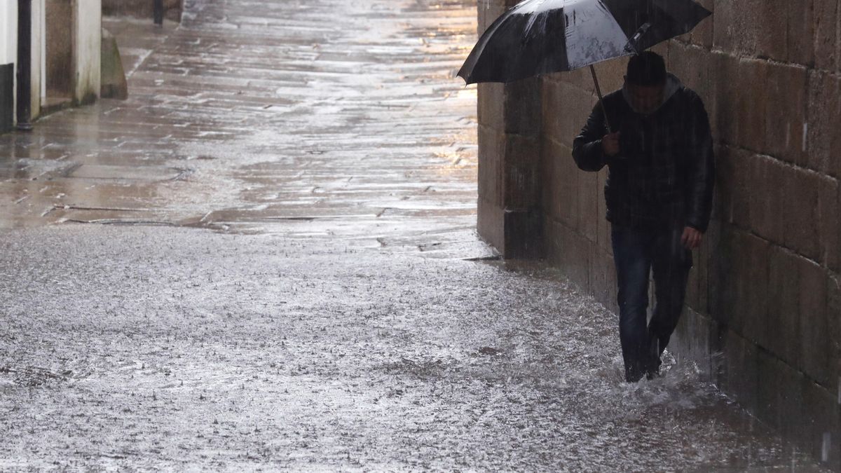 Un hombre se cubre de la lluvia con un paraguas mientras pasea por una calle
