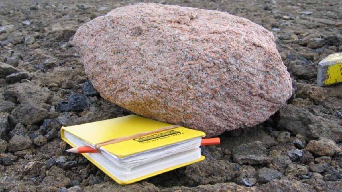 Una roca de granito rosa junto a un cuaderno amarillo como referencia