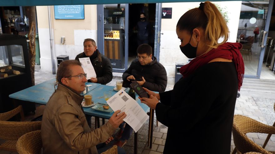 Una camarera pide certificado a los clientes en la terraza de un bar.