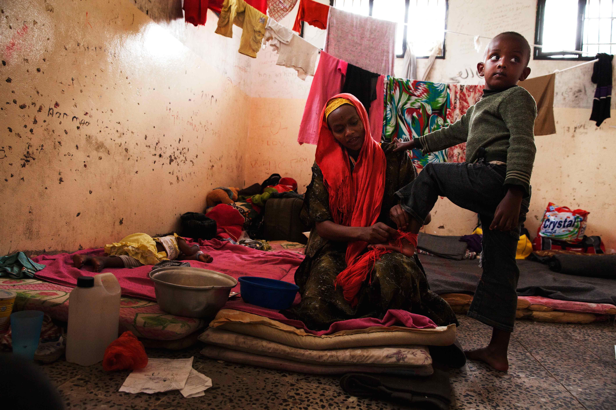 Rumana, inmigrante víctima del tráfico de personas en Yemen, ingresado en el centro de detención de Saná. En la imagen aparece calzando uno de sus hijos junto a los que espera regresar a su país en el centro de detención. / Copyright: Anna Surinyach/MSF