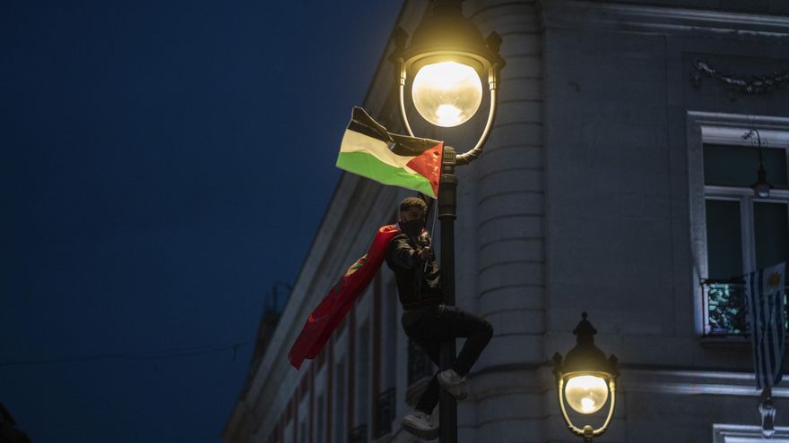 Un manifestante ondea la bandera palestina desde una farola en la Puerta del Sol