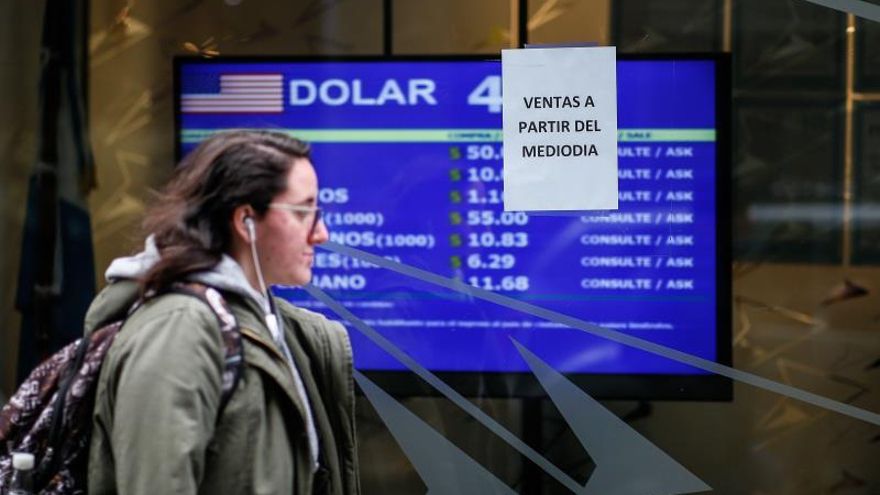 Una mujer fue registrada este lunes al caminar frente a un tablero que muestra los valores de cambio del dólar, en Buenos Aires (Argentina).