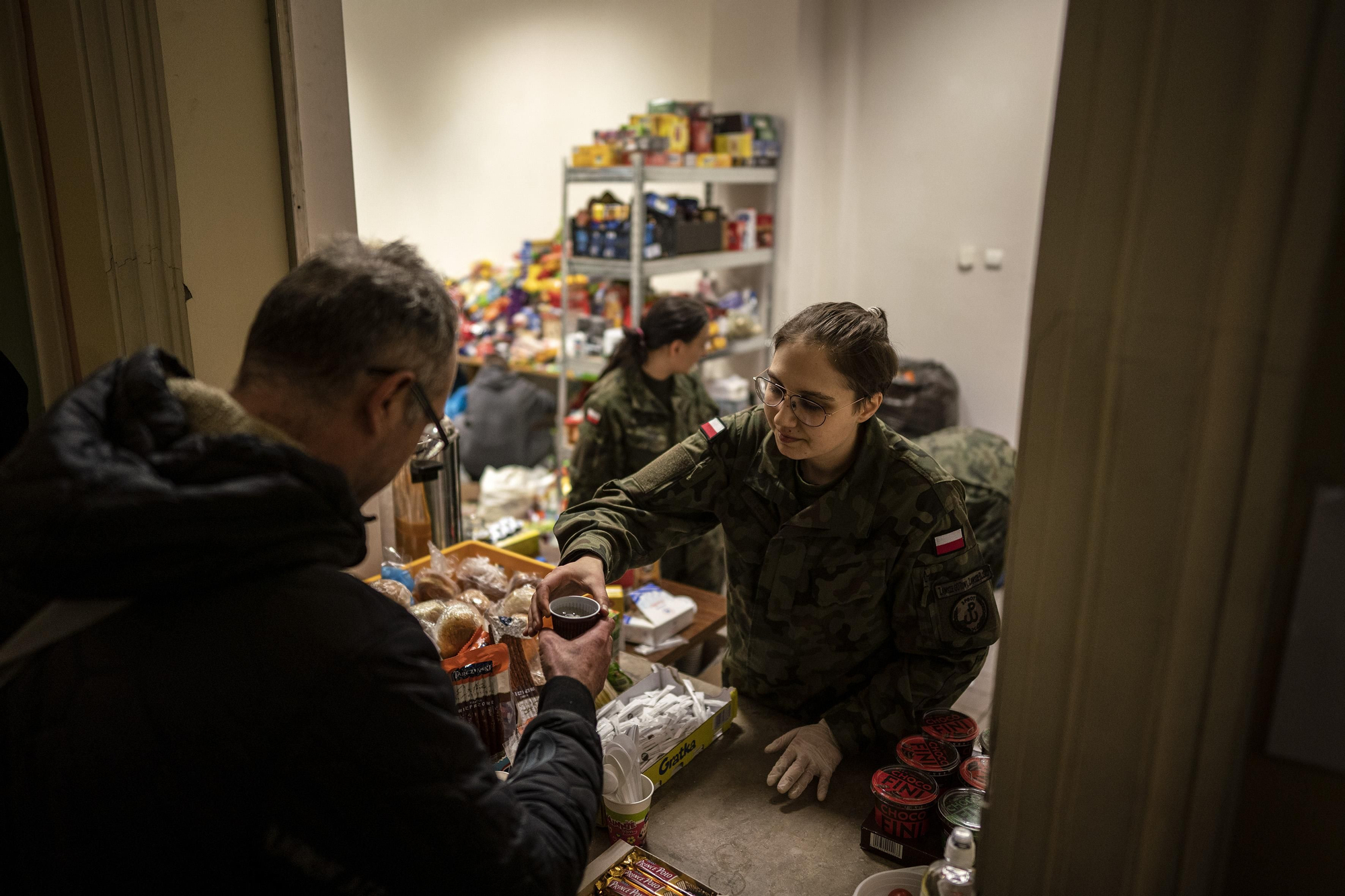 Colaboradores con petos amarillos y naranjas reparten mantas, bebidas calientes, bollos, pañales o muñecos de peluche entre los ojerosos rostros de los refugiados.
