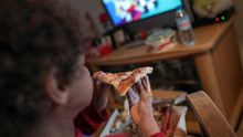 Un niño come un trozo de pizza del menú infantil de Telepizza mientras ve la televisión en su casa