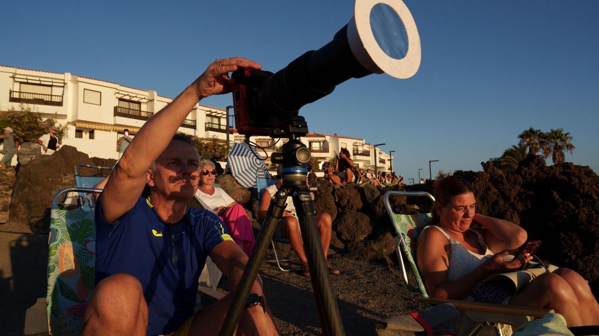 Varias personas contemplan desde la playa el eclipse solar, que se ha visto de forma parcial, este miércoles en el municipio tinerfeño de Guía de Isora.