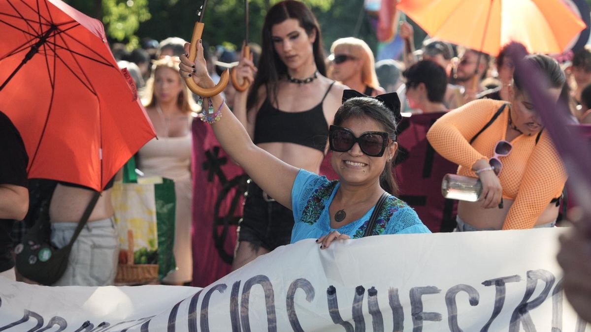 Una joven sonríe tras una de las pancartas mientras sujeta un paraguas de color naranja, que muchos asistentes han utilizado para hacer frente al sol.