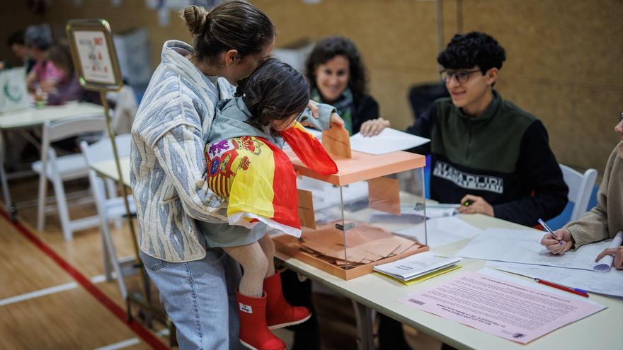 Una mujer vota de la mano de su hija vestida con la bandera de España en el Colegio San Agustín de Madrid