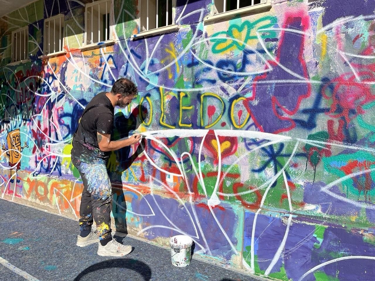 Un artista de Boa Mistura marcando en blanco sobre el mural las ramas de el árbol de los sueños