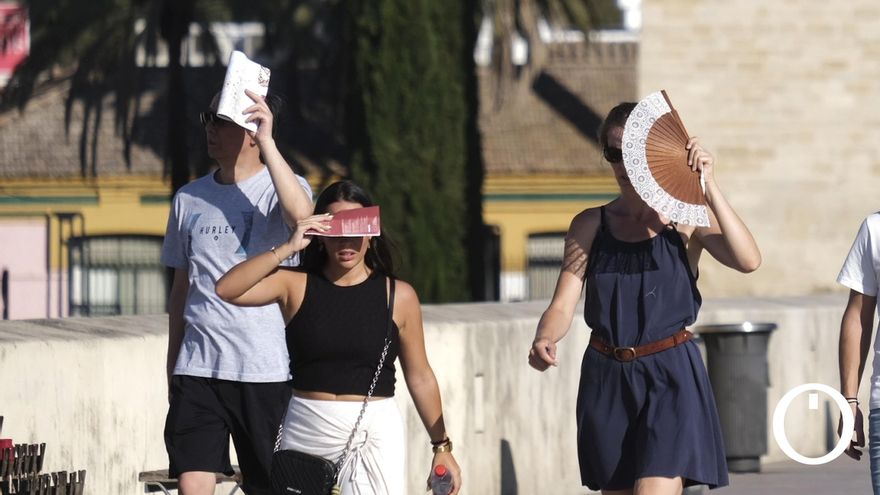 Cordobeses protegiéndose del sol al cruzar el Puente Romano