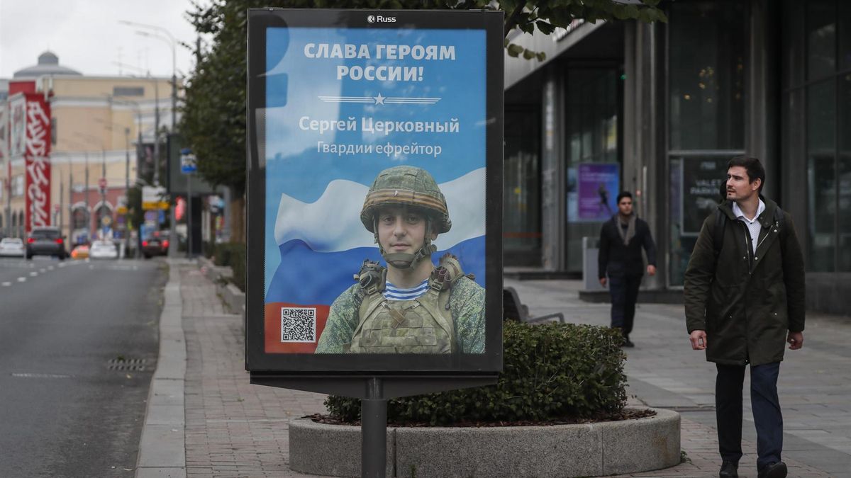 Dos hombres pasan junto a un cartel que muestra a un soldado y el lema "Gloria a los Héroes de Rusia".