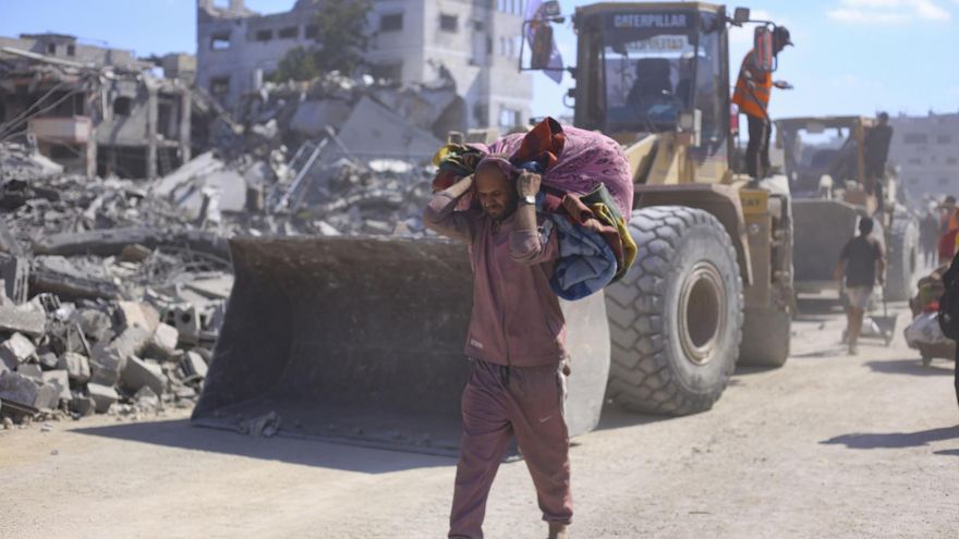 Un hombre con un hatillo con sus pertenencias pasa ante varias excavadoras del Ayuntamiento de la ciudad de Gaza que comienza este martes las operaciones de remoción de escombros y apertura de las calles principales de la capital gazatí para despejarlas y prepararlas para su uso, tras dos años de bombardeos.
