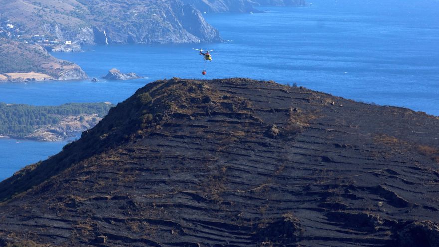Un helicóptero se dispone a refrescar la superficie afectada por el incendio en el parque natural de Cap de Creus (Girona).