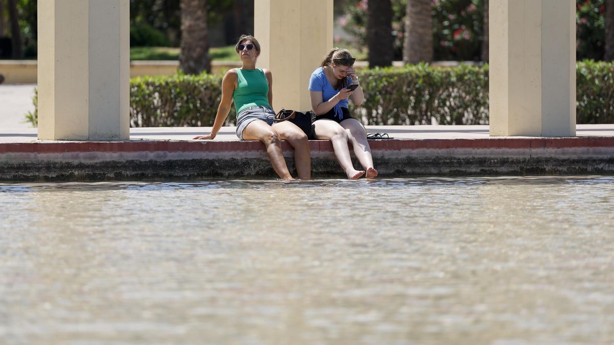 Dos personas se refrescan en una fuente de los jardines del antiguo cauce del Turia para combatir el calor