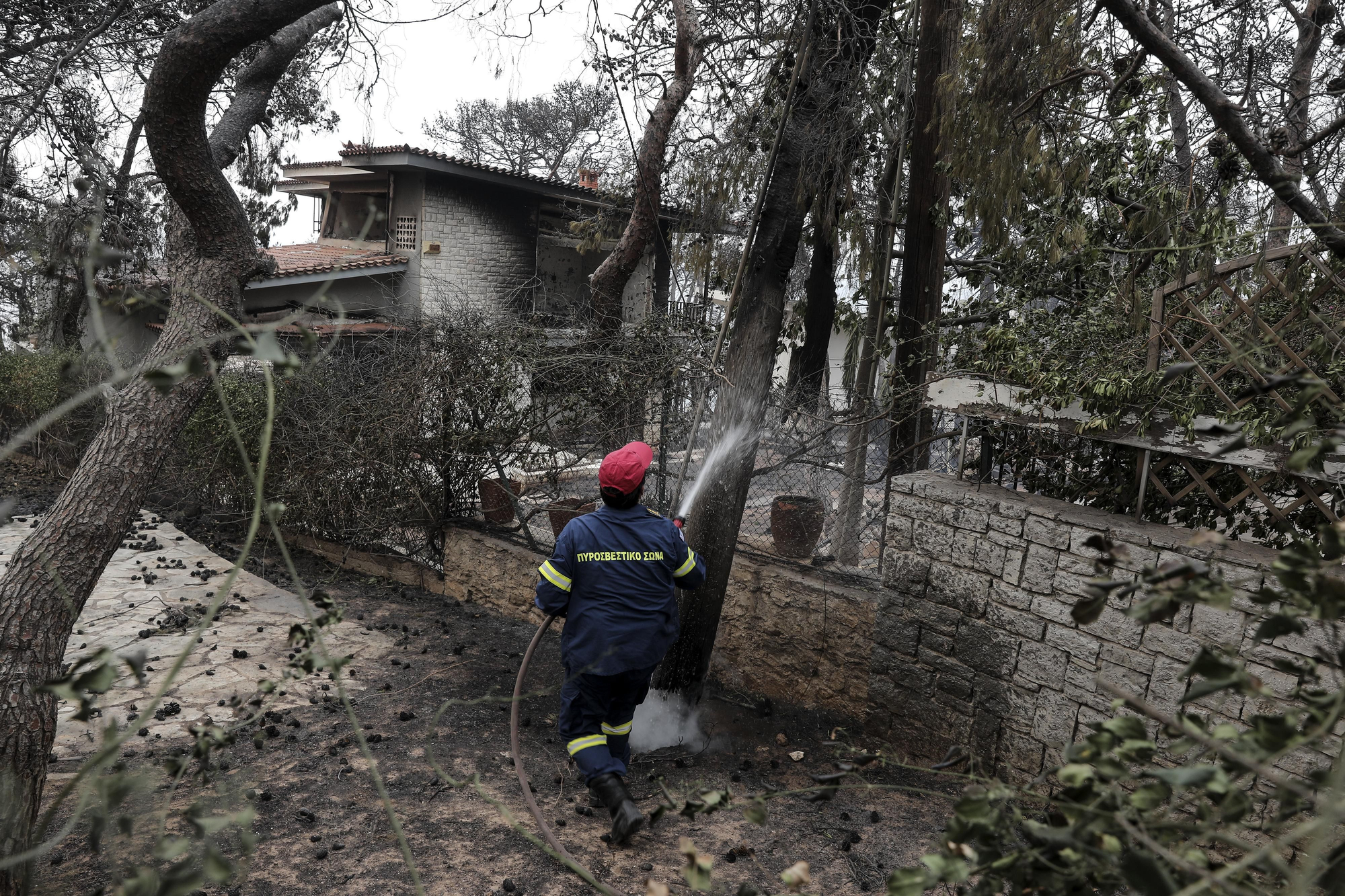 Un bombero apaga el fuego en el exterior de una casa incendiada en la localidad de Kineta, al oeste de Atenas