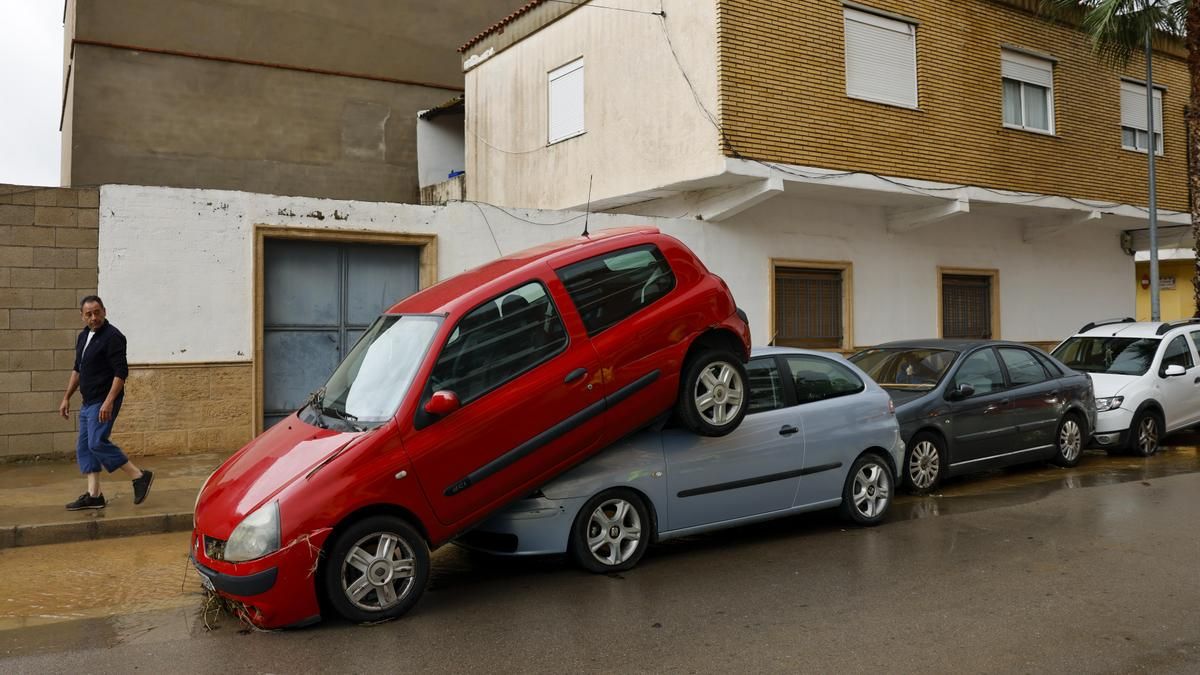 Una persona pasa junto a unos coches amontonados debido a las lluvias torrenciales que afectan a la Comunitat Valenciana, y especialmente a la provincia de Valencia, en la que se ha establecido el aviso rojo.