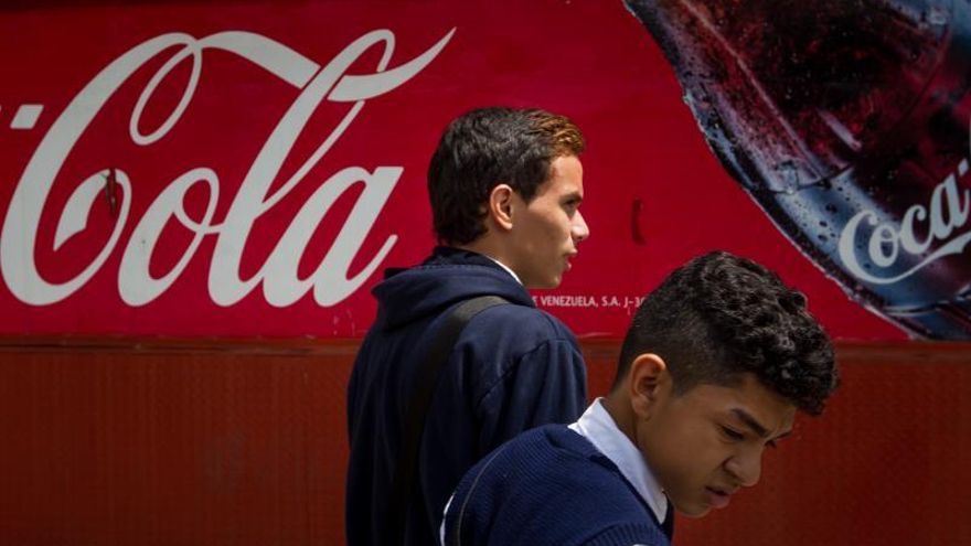 Dos hombres caminan junto a un kiosco de Coca-Cola.