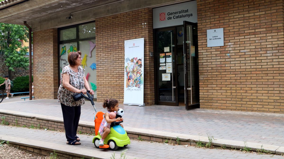 Una mujer pasea a una niña frente a la ludoteca de Salt (Girona)