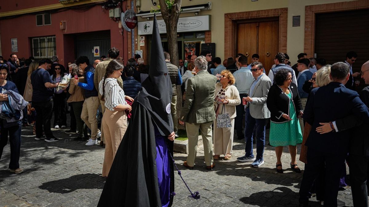 Un nazareno de San Bernardo pasa junto a grupos de personas consumiendo en la calle en Sevilla.