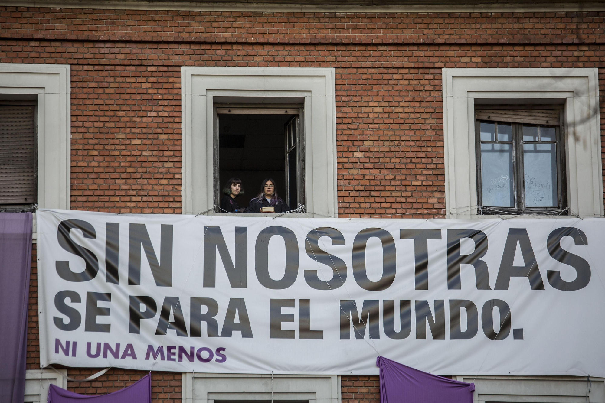 Un grupo de activistas feministas contemplan el arranque de la marcha de Madrid desde un balcón del centro social autogestionado la Ingobernable