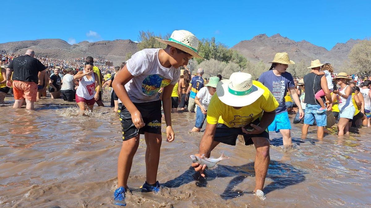 Un hombre atrapa una lisa en plena festividad de El Charco, bajo la atenta mirada de su hijo.