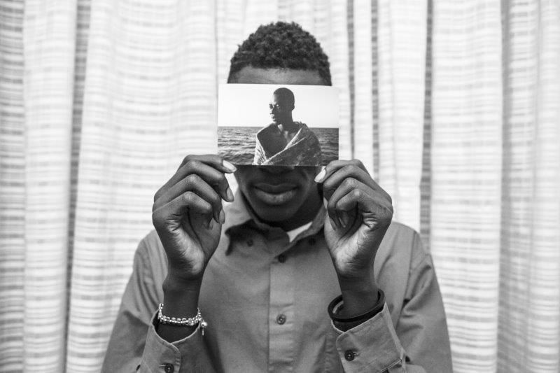 Malick posa para un retrato dentro de su habitación del Hotel Colibri, sosteniendo un retrato suyo