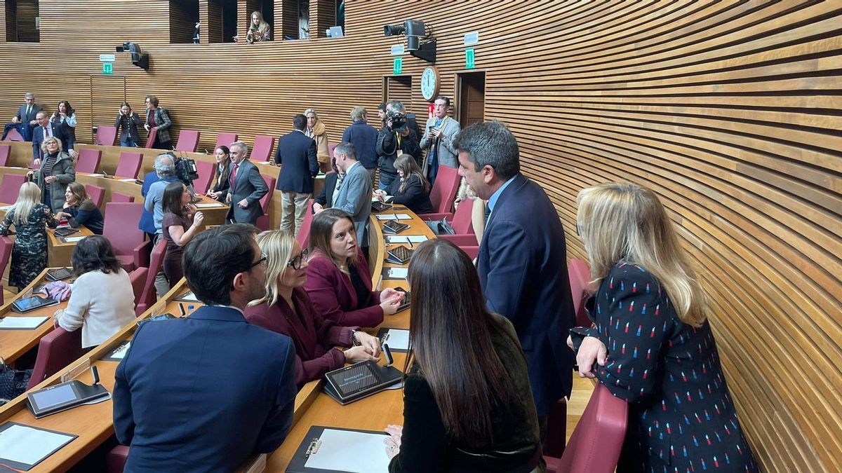 Mazón saludando a diversos diputados en su escaño ubicado en la última fila.