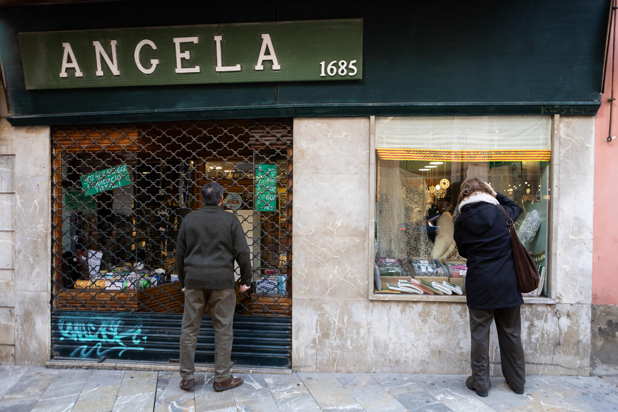 Dos paseantes, asomándose a Ca Donya Àngela, ya cerrada