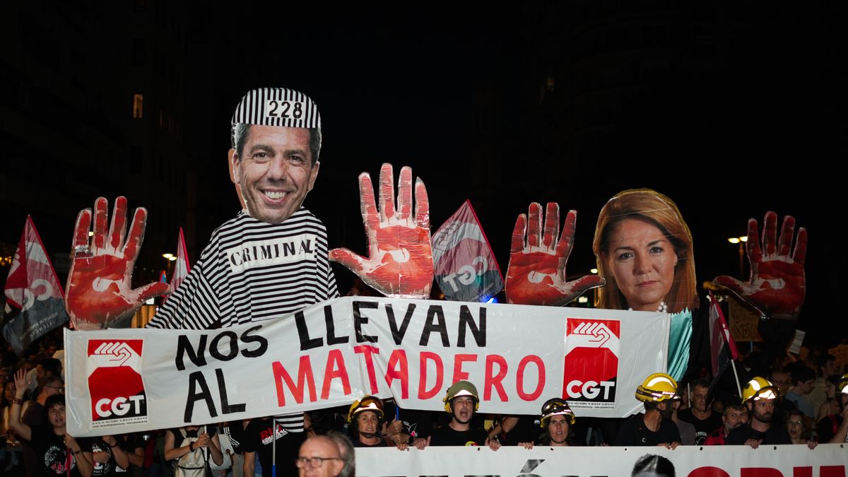 Detalle de un cartel-collage de Carlos Mazón con un gorro de preso con el número de 228 y las manos rojas