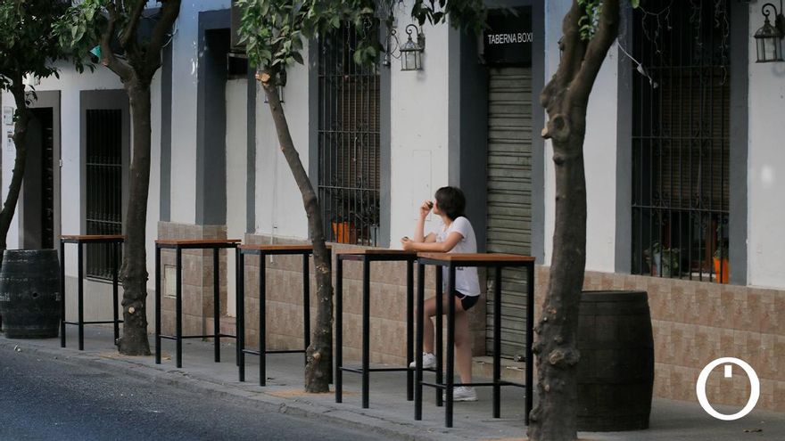 Una mujer espera en una terraza de un bar cerrado a mediodía