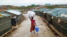 Una joven rohingya camina por las calles mojadas del campo de refugiados de Balukhali portando sobre su cabeza artículos de primera necesidad suministrados por la ONU.