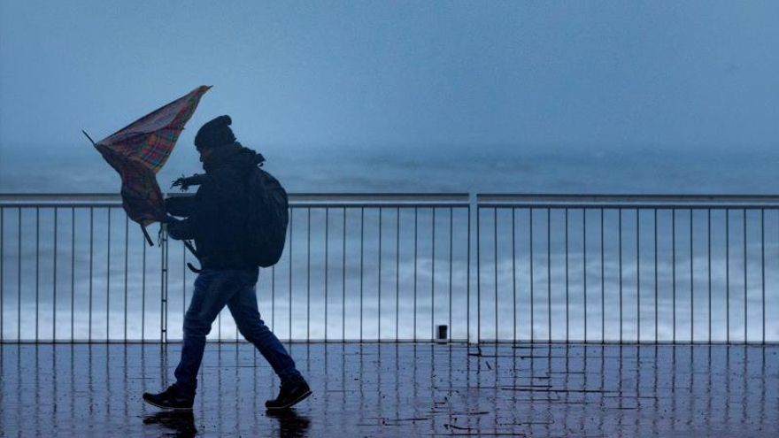 Un hombre pasea con un fuerte viento por la playa de la Barceloneta.