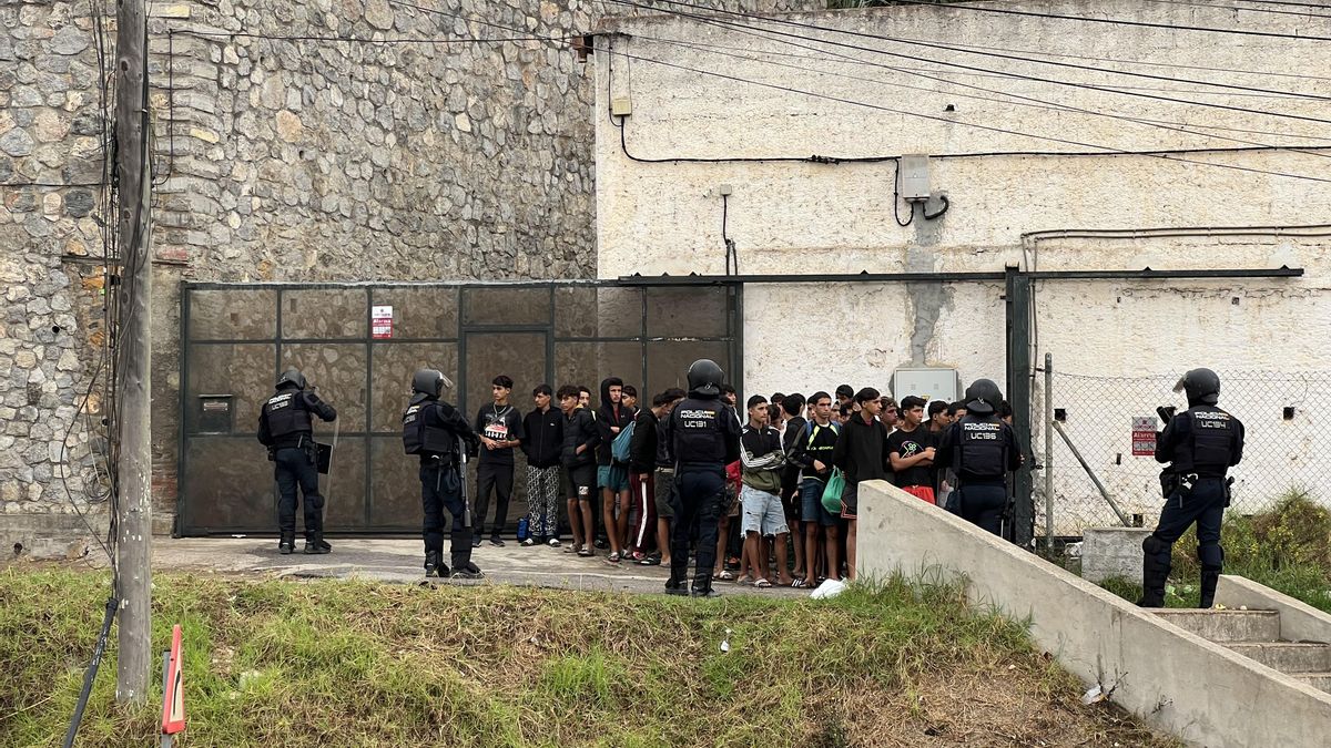 Un grupo de menores migrantes apartados al margen del operativo policial para desalojar la Playa del Trampolín, en Ceuta, esperan su traslado