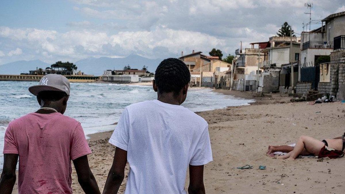 Dos menores de Gambia que cruzaron el Mediterráneo sin sus padres caminan en una playa de Italia.