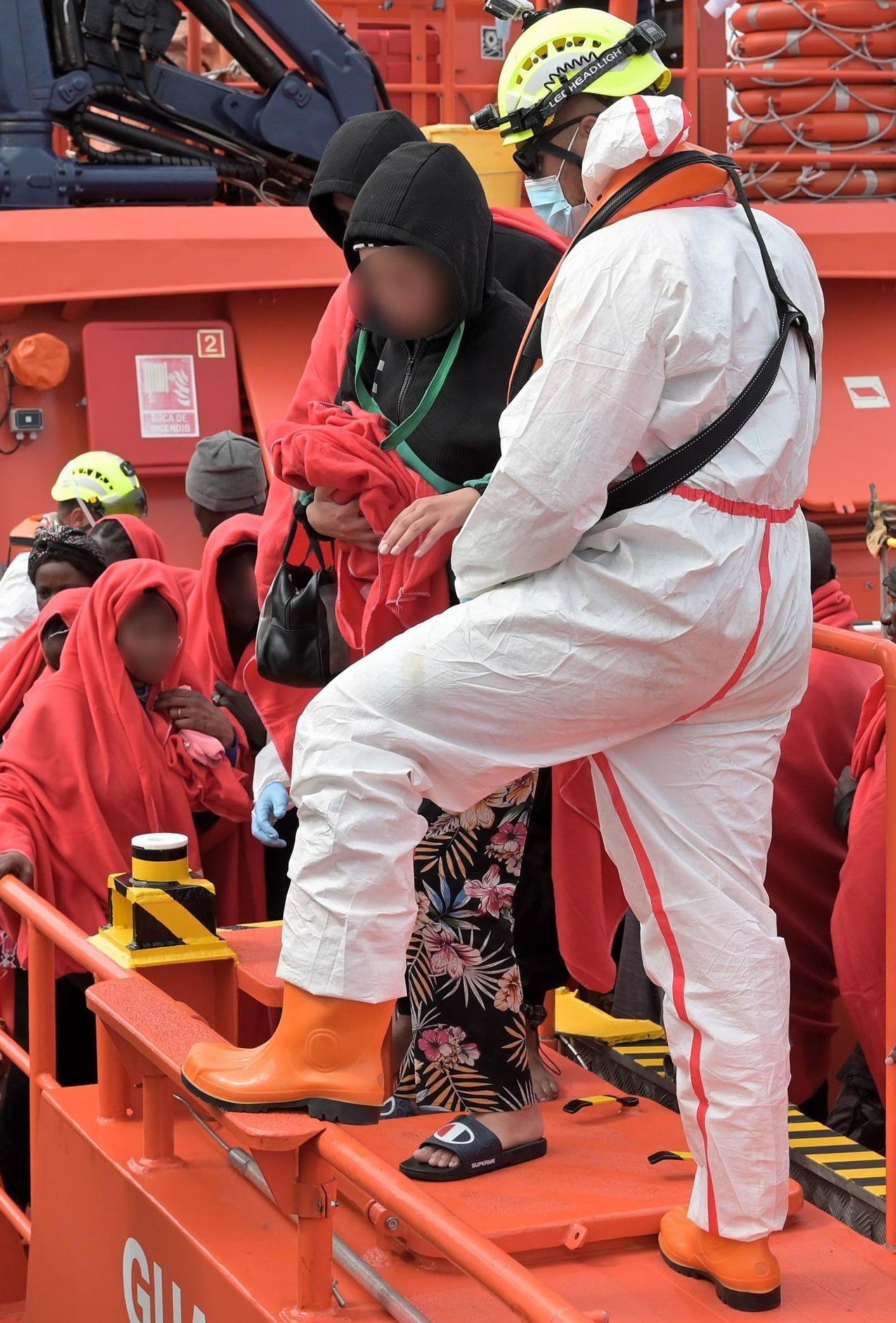 En la imagen, el personal de Salvamento ayuda a bajar del barco a una de las mujeres, que llevaba consigo dos gatos arropados en una manta. 