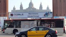 Un autobús de TMB passa davant d'un cartell del Mobile a la plaça Espanya de Barcelona