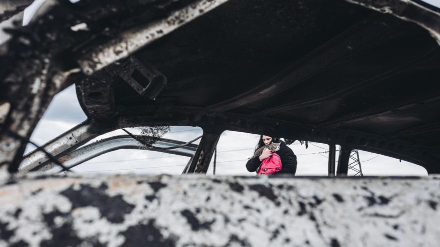 Una joven y su gato caminan frente a un coche calcinado, a 7 de marzo de 2022, en Irpin (Ucrania).