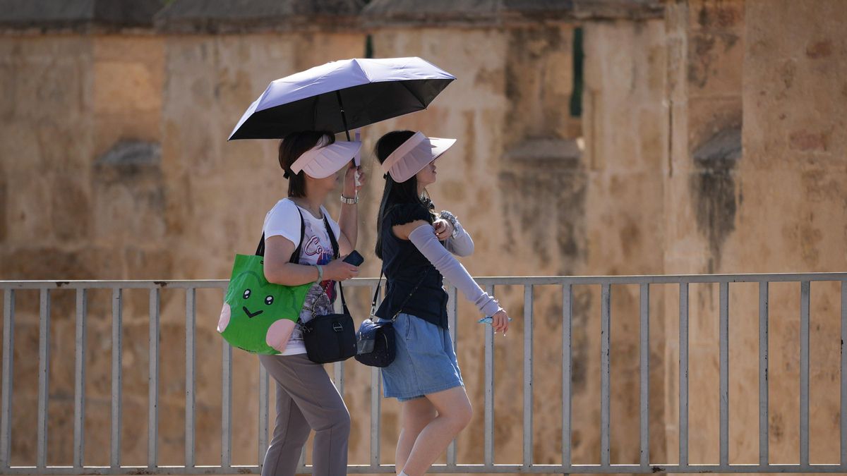 Dos turistas se protegen del sol con un paraguas.