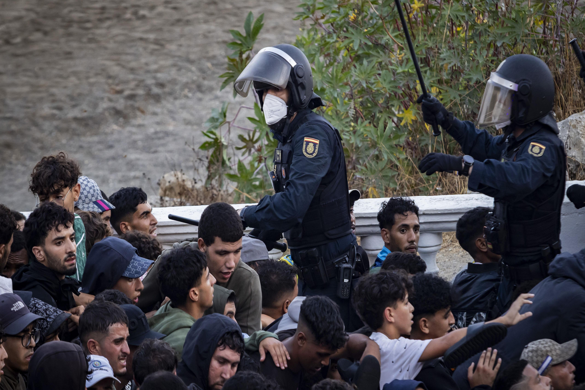 Dos agentes blanden las porras mientras los jóvenes que esperan para marchar empujan para superar el cordón.