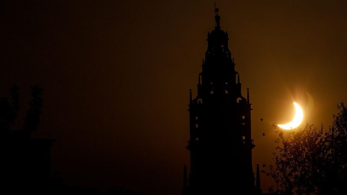 Varios pájaros al vuelo junto a la torre de la Mezquita Catedral y el eclipse.