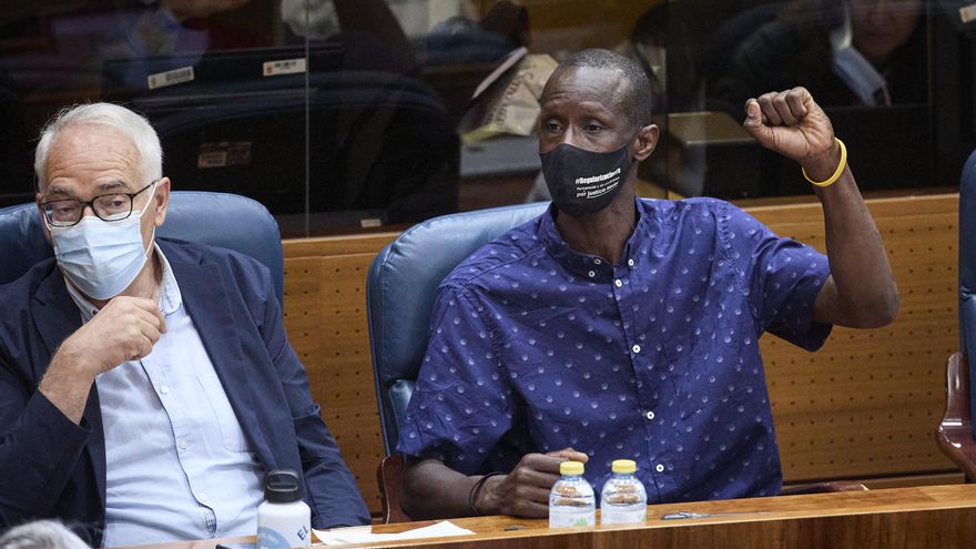 El portavoz del sindicato de manteros y miembro de la Asociación de los Sin Papeles, Serigne Mbaye (d), levanta el brazo en la segunda sesión del pleno de investidura de la presidenta en funciones de la Comunidad y candidata a la reelección, Isabel Díaz Ayuso