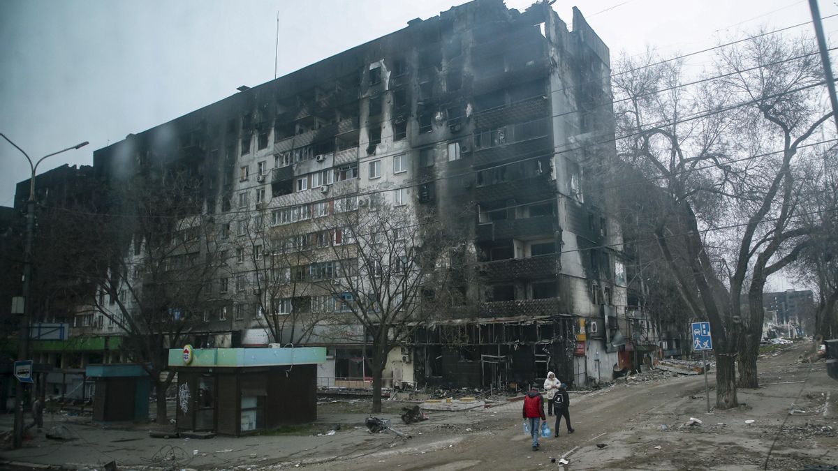 Una foto tomada durante una visita a Mariupol organizada por el ejército ruso muestra a la población local en busca de agua potable cerca de edificios de apartamentos destruídos y quemados en el centro.