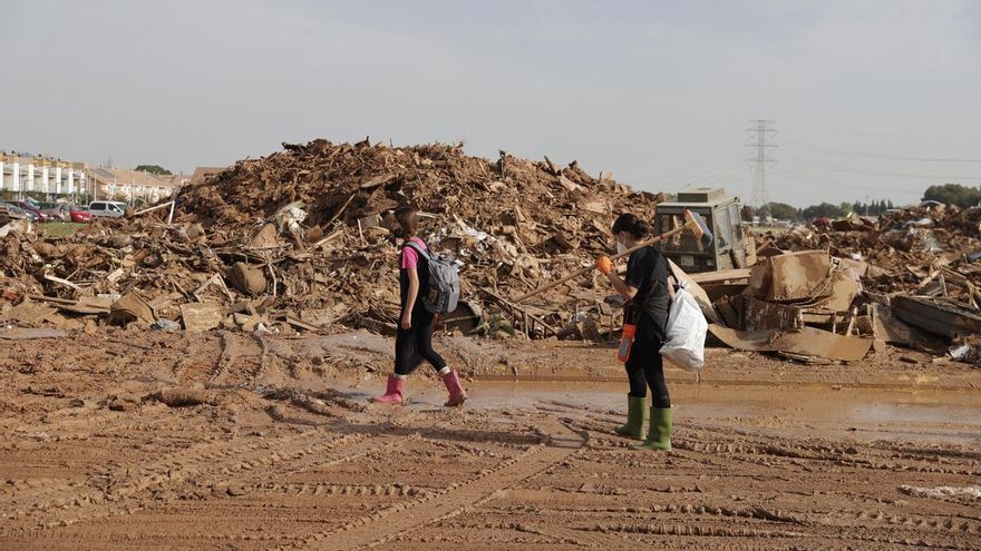 Dos mujeres caminan frente a una gran montaña de escombros, este martes en Paiporta (Valencia).