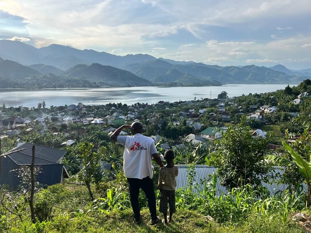 Un miembro de MSF y un niño contemplan la ciudad de Minova y el lago Kivu desde lo alto de una colina en la provincia de Kivu del Sur, República Democrática del Congo.