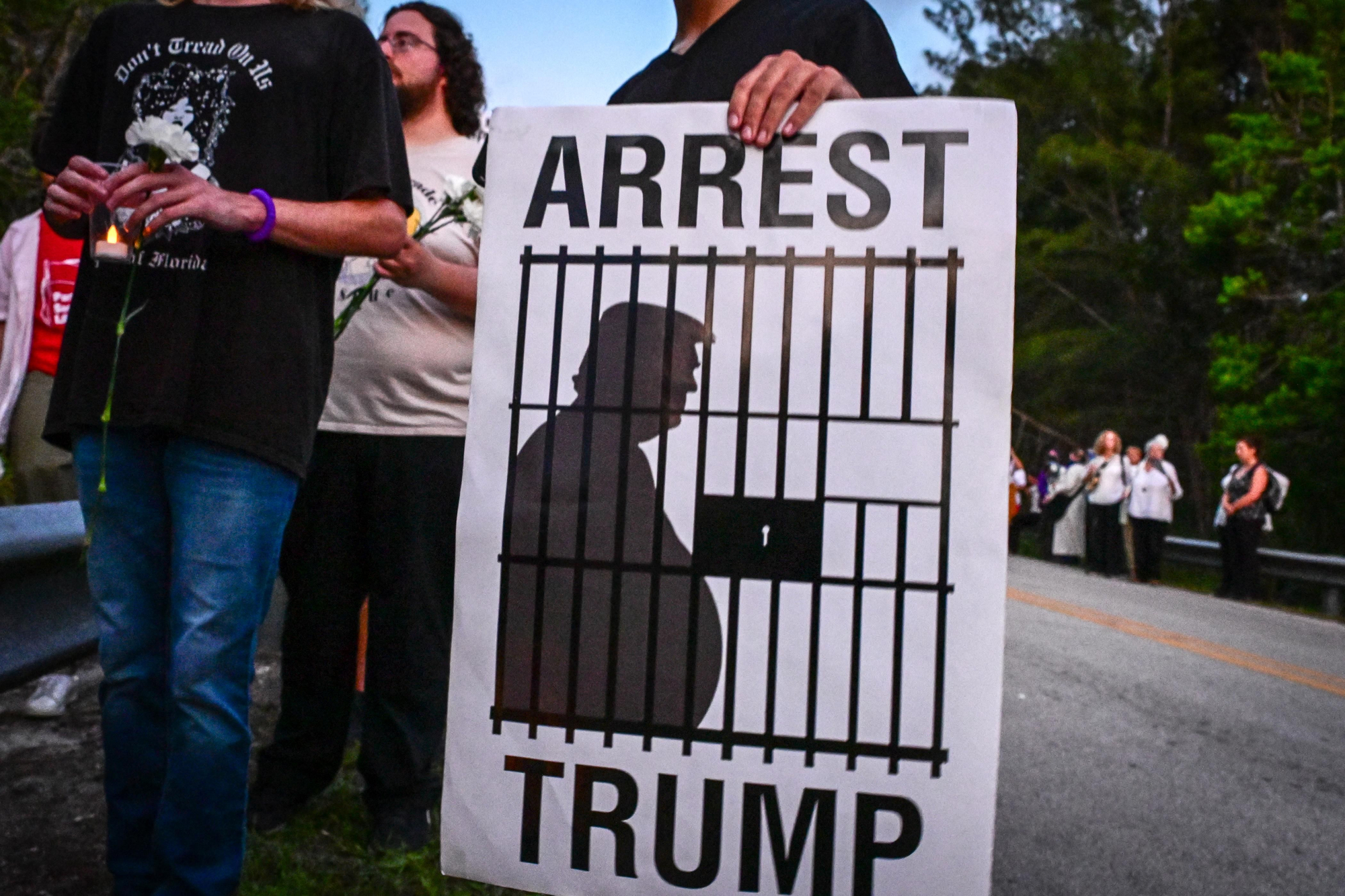 Una persona sostiene un cartel que dice "Arrestar a Trump", durante una vigilia frente al Centro de Detención Krome en Miami el 24 de mayo de 2025, en protesta contra la detención y las deportaciones masivas del Servicio de Inmigración y Control de Aduanas de Estados Unidos (ICE).