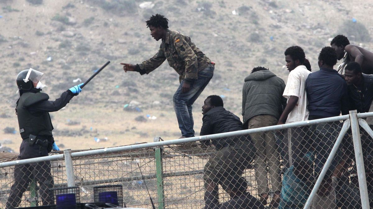 Un guardia civil apunta con la porra a un inmigrante en lo alto de la valla de Melilla / AP